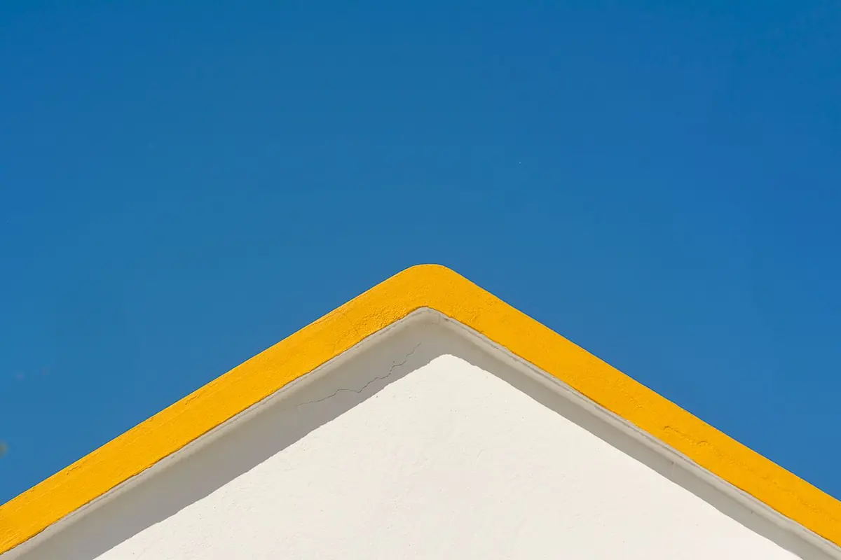 A white gable end with yellow-painted fascia trim against a blue sky