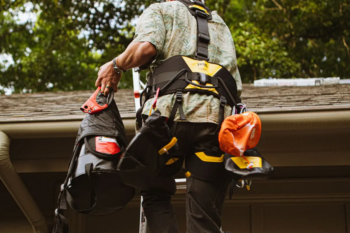 A roofer with a tool belt climbing a ladder to a house roof