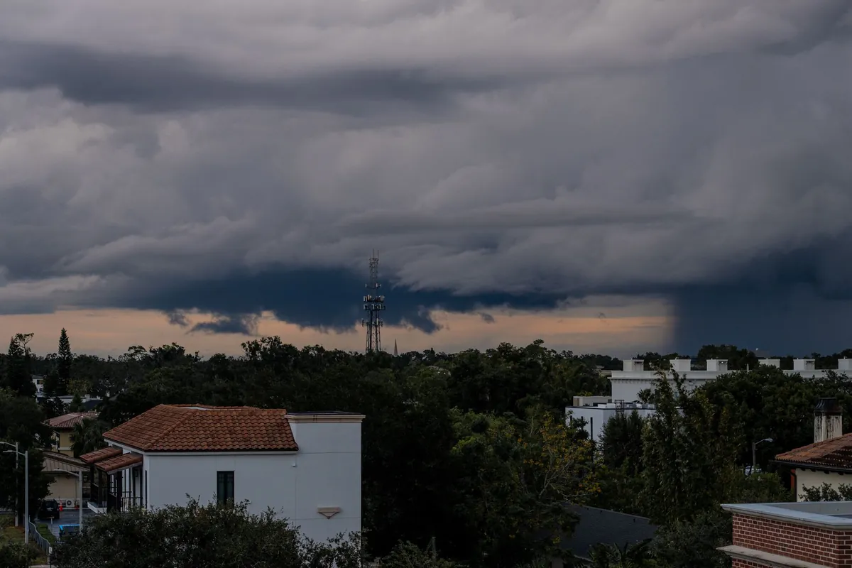 A dark storm cell building over white stucco homes with clay tile roofs