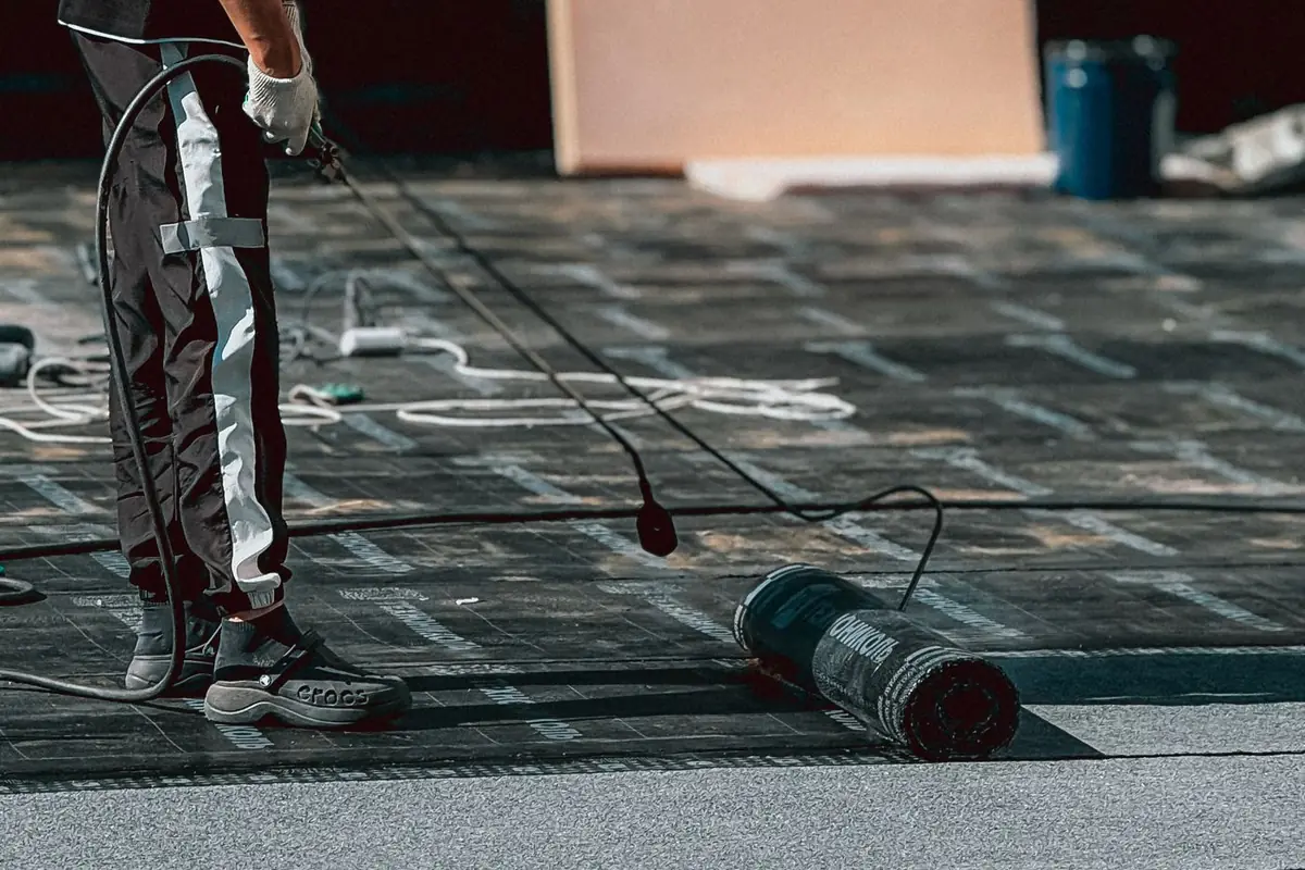 A worker applying a waterproof coating to a flat roof with a long-handled roller