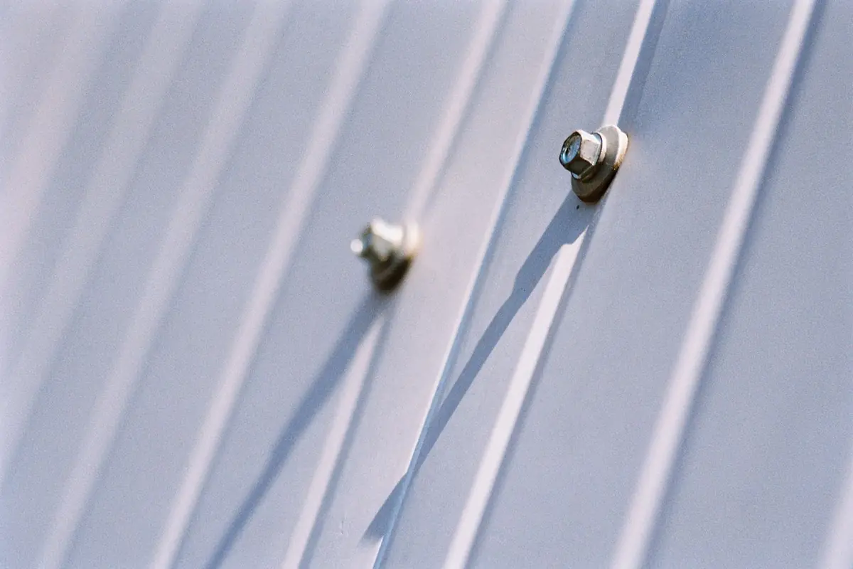 Close-up of hex-head fasteners with washers on a light gray corrugated metal roof panel